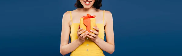 Частковий вид усміхненої дівчини, що тримає подарунок ізольовано на синьому — стокове фото