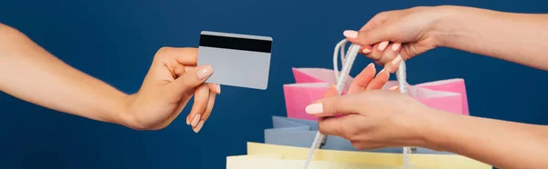 Vista cortada de mulheres segurando sacos de compras e cartão de crédito isolado em azul — Fotografia de Stock