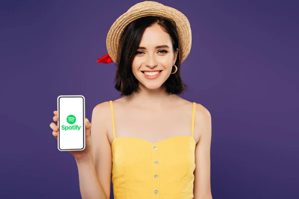 Київ, Україна-3 липня 2019: усміхнена дівчина в солом'яному капелюсі тримає смартфон з додатком Spotify, ізольованим на фіолетовому — стокове фото