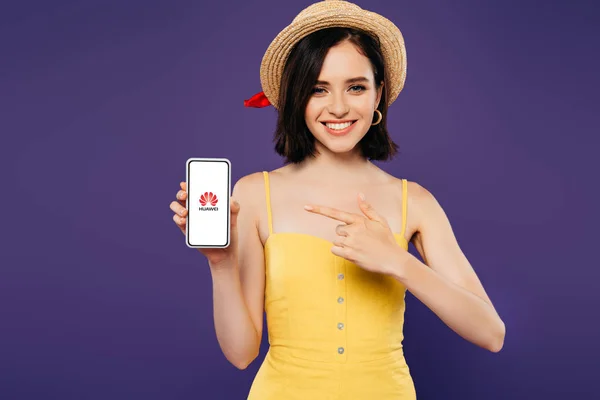 Kyiv, ukraine - 3. Juli 2019: lächelndes Mädchen mit Strohhut, das mit dem Finger auf ein Smartphone mit Huawei-Logo zeigt — Stockfoto