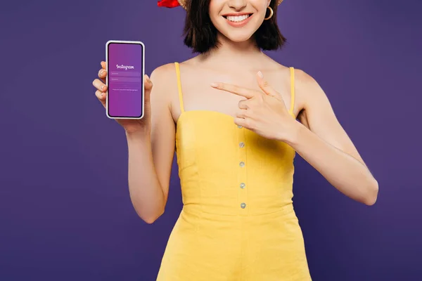 KYIV, UKRAINE - JULY 3, 2019: cropped view of girl in straw hat pointing with finger at smartphone with instagram app isolated on purple — Stock Photo