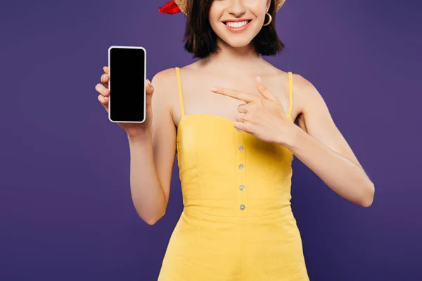 Vue recadrée de fille en chapeau de paille pointant avec le doigt sur le smartphone avec écran vide isolé sur violet — Photo de stock