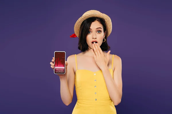 Girl in straw hat showing idea gesture and holding smartphone with trading courses app isolated on purple — Stock Photo