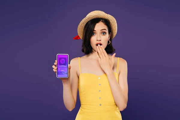 Девушка в соломенной шляпе показывает жест идеи и проведение смартфона с приложением для покупок изолированы на фиолетовый — стоковое фото