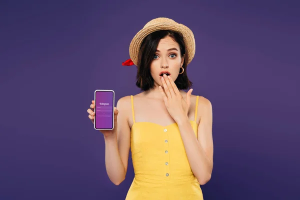 KYIV, UCRAINA - LUGLIO 3, 2019: ragazza in cappello di paglia che mostra il gesto dell'idea e tiene lo smartphone con l'app Instagram isolata sul viola — Foto stock
