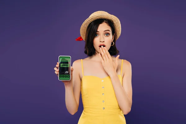 Chica en sombrero de paja que muestra el gesto de la idea y la celebración de teléfono inteligente con aplicación de reserva aislado en púrpura - foto de stock