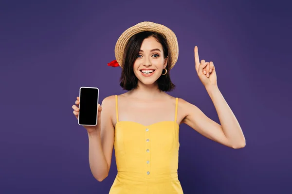 Aufgeregtes Mädchen mit Strohhut zeigt Ideengeste und hält Smartphone mit leerem Bildschirm isoliert auf lila — Stockfoto