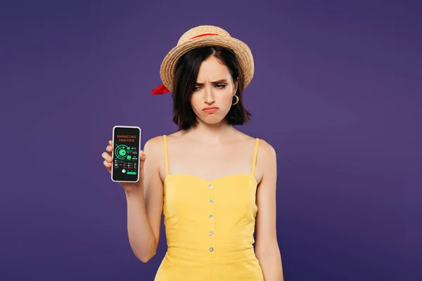 Sad pretty girl in straw hat holding smartphone with marketing analysis app isolated on purple — Stock Photo