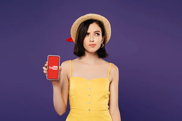 KYIV, UKRAINE - JULY 3, 2019: dreamy pretty girl in straw hat holding smartphone with youtube app isolated on purple — Stock Photo