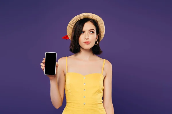 Verträumte hübsche Mädchen mit Strohhut hält Smartphone mit leerem Bildschirm isoliert auf lila — Stockfoto