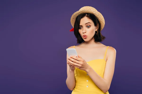 Surprised pretty girl in straw hat using smartphone isolated on purple — Stock Photo