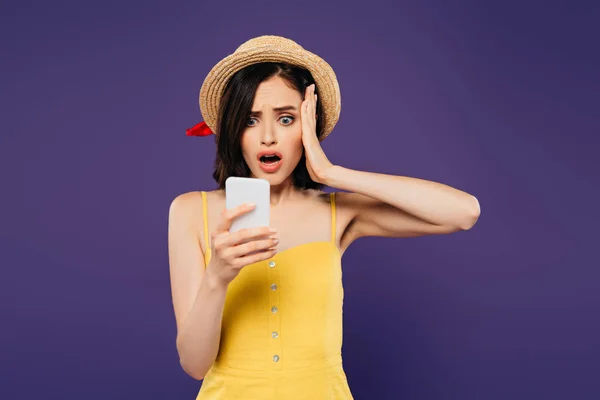 Chocado menina bonita em chapéu de palha usando smartphone isolado em roxo — Fotografia de Stock