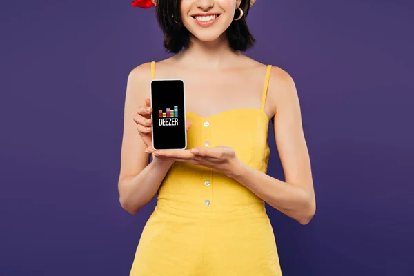 KYIV, UCRAINA - LUGLIO 3, 2019: vista ritagliata della ragazza sorridente che tiene lo smartphone con l'app deezer isolata sul viola — Foto stock