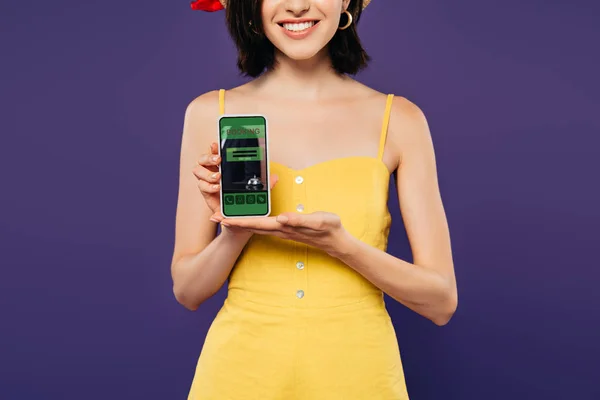 Vista cortada de menina sorridente segurando smartphone com aplicativo de reserva isolado em roxo — Fotografia de Stock