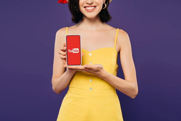 Vista cortada de menina sorridente segurando smartphone com aplicativo isolado em roxo — Fotografia de Stock