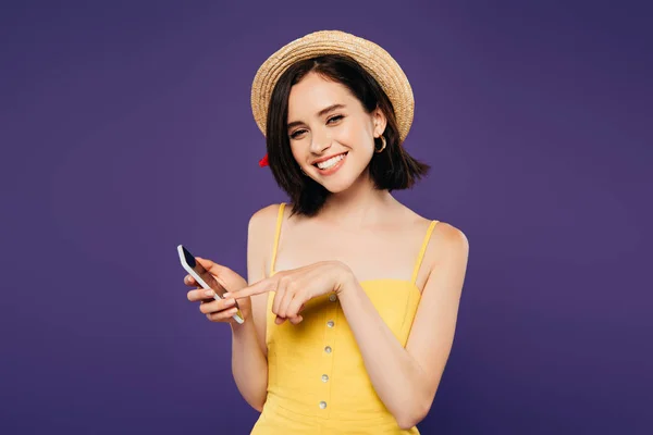Sorrindo menina bonita em chapéu de palha segurando smartphone isolado em roxo — Fotografia de Stock