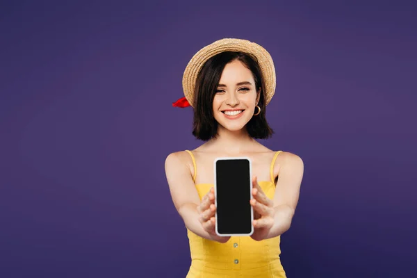 Foyer sélectif de sourire jolie fille en chapeau de paille présentant smartphone avec écran blanc isolé sur violet — Photo de stock