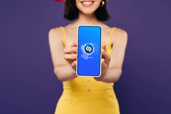 KYIV, UKRAINE - JULHO 3, 2019: foco seletivo de menina sorridente apresentando smartphone com aplicativo shazam isolado em roxo — Fotografia de Stock