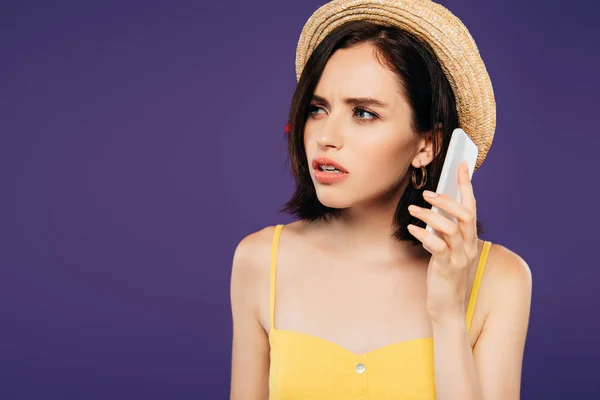 Preocupado menina bonita em chapéu de palha falando no smartphone isolado em roxo — Fotografia de Stock