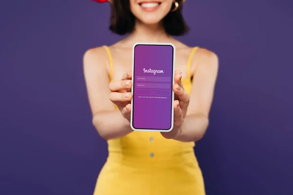 KYIV, UCRANIA - 3 de julio de 2019: enfoque selectivo de la chica sonriente que presenta el teléfono inteligente con aplicación instagram aislado en púrpura - foto de stock