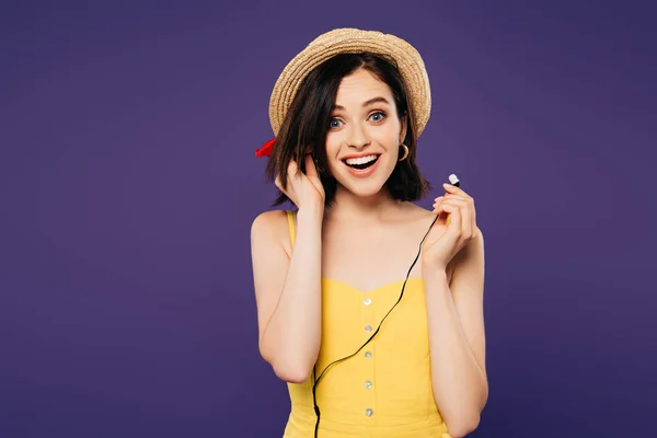 Excited smiling pretty girl in straw hat putting on earphones isolated on purple — Stock Photo