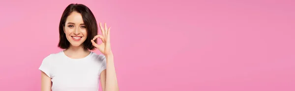Colpo panoramico di sorridente bella ragazza mostrando segno ok isolato su rosa — Foto stock