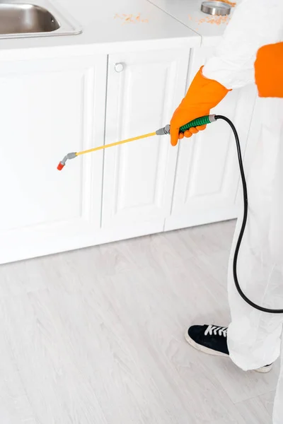 Cropped view of exterminator in uniform standing with toxic spray near kitchen cabinet — Stock Photo