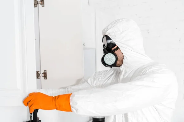 Exterminador em máscara protetora e uniforme de pé perto do armário da cozinha — Fotografia de Stock