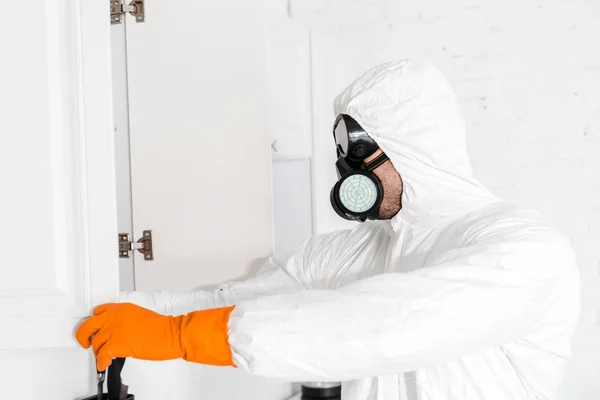 Disinfestatore in maschera protettiva e uniforme in piedi vicino armadio da cucina — Foto stock