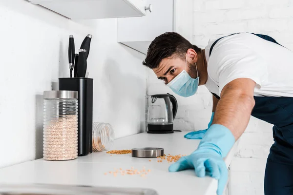 Exterminador de pé perto do armário da cozinha e olhando para a mesa com frascos — Fotografia de Stock