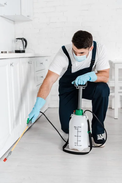 Exterminador en máscara protectora que sostiene el aerosol tóxico cerca del gabinete de cocina - foto de stock