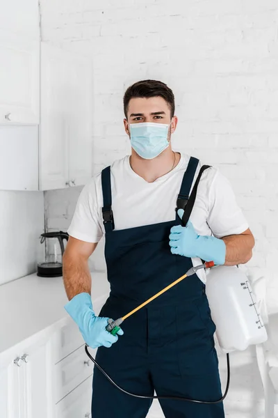 Exterminator in protective mask and uniform holding toxic spray and looking at camera — Stock Photo