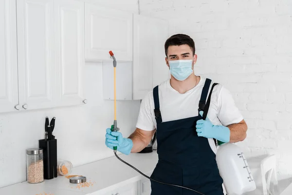 Exterminador sosteniendo spray tóxico cerca de la mesa con frascos en la cocina - foto de stock