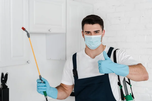 Exterminador em uniforme segurando spray tóxico e mostrando polegar para cima — Fotografia de Stock