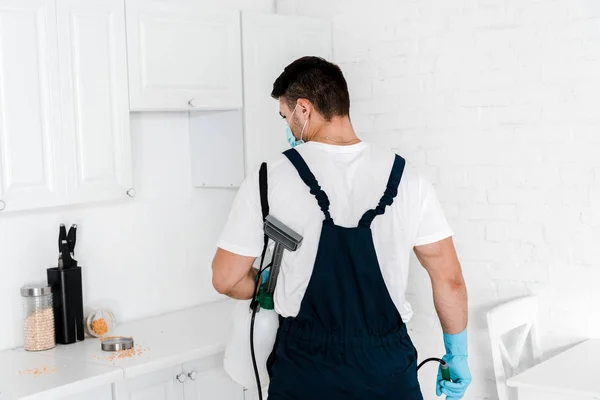 Exterminator holding toxic spray and looking at table with jars in kitchen — Stock Photo