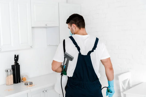 Sterminatore in possesso di spray tossico e guardando tavolo con vasi in cucina — Foto stock