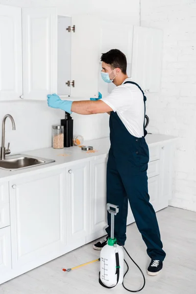 Sterminatore in piedi vicino armadio da cucina e attrezzature tossiche sul pavimento — Foto stock