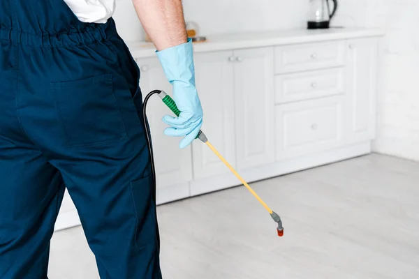 Cropped view of exterminator in uniform holding spray with pesticide near kitchen cabinet — Stock Photo