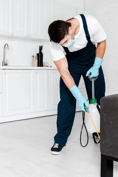 Hombre en uniforme y guantes de látex azul sosteniendo aerosol con pesticida - foto de stock