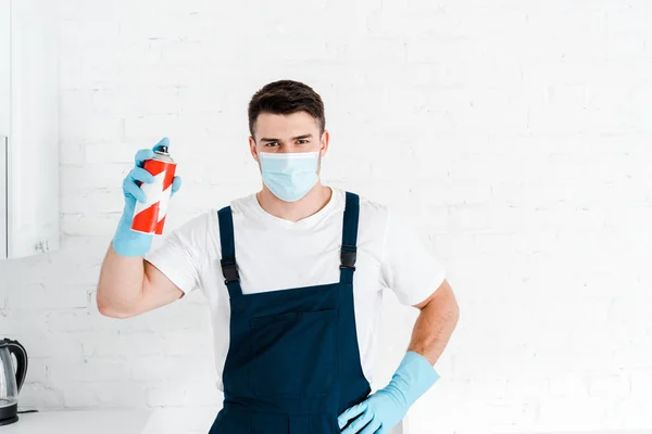 Exterminator in latex gloves holding toxic spray can and standing with hand on hip — Stock Photo