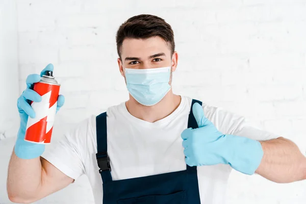 Exterminador en guantes de látex sosteniendo lata de spray tóxico y mostrando el pulgar hacia arriba - foto de stock