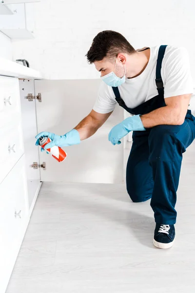 Exterminator in blue latex gloves holding spray can near kitchen cabinet — Stock Photo