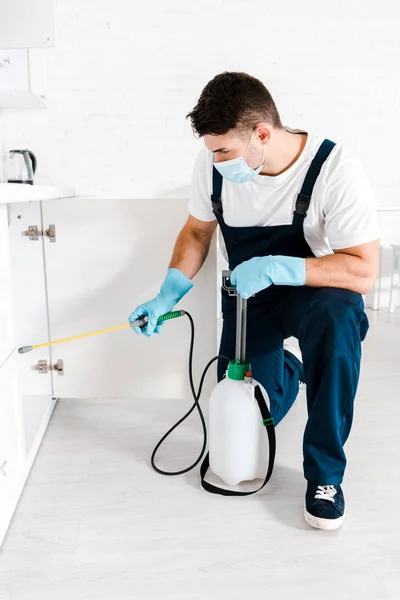 Homem em máscara protetora segurando spray tóxico perto de baratas no chão na cozinha — Fotografia de Stock