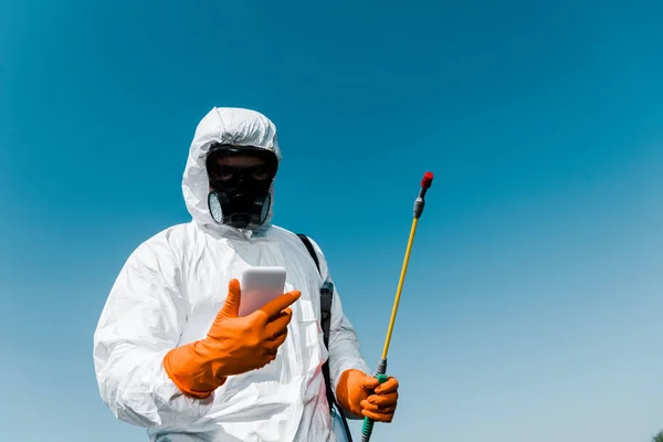 Exterminador usando teléfono inteligente mientras mantiene spray contra el cielo - foto de stock