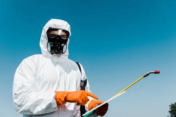 Man in protective mask and uniform pointing with finger at digital tablet against blue sky — Stock Photo