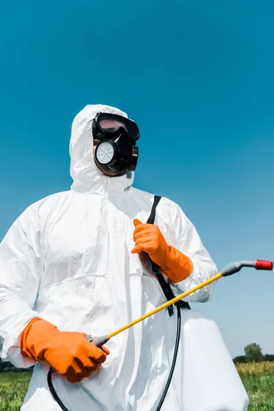 Exterminador en guantes de látex naranja con spray tóxico contra el cielo - foto de stock