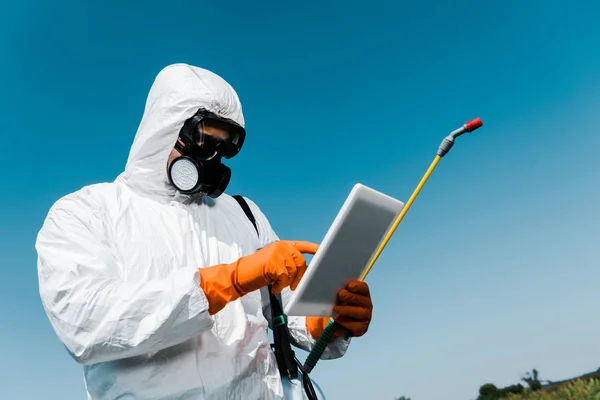 Homme en masque de protection et pointage uniforme avec le doigt à la tablette numérique contre le ciel — Photo de stock