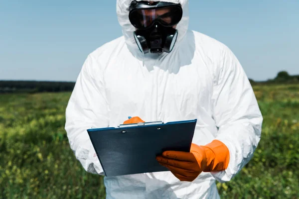 Hombre con máscara protectora y escritura uniforme mientras sostiene el portapapeles - foto de stock