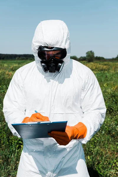 Exterminador en máscara protectora y escritura uniforme mientras sostiene el portapapeles - foto de stock