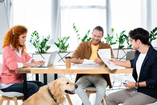 Amis souriants faire de la paperasse et en utilisant un ordinateur portable dans le bureau — Photo de stock